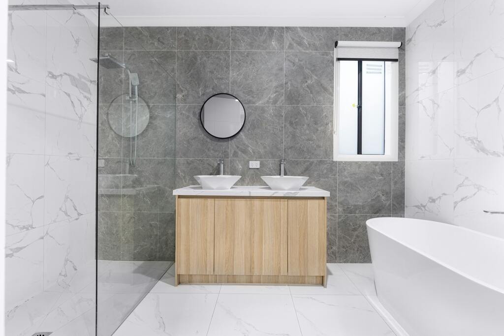 Wooden bathroom vanity with grey tiled walls and a white stand alone bath.