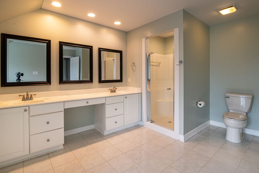 A spacious bathroom with a large white vanity with drawers. Completed by three mirros and a shower.
